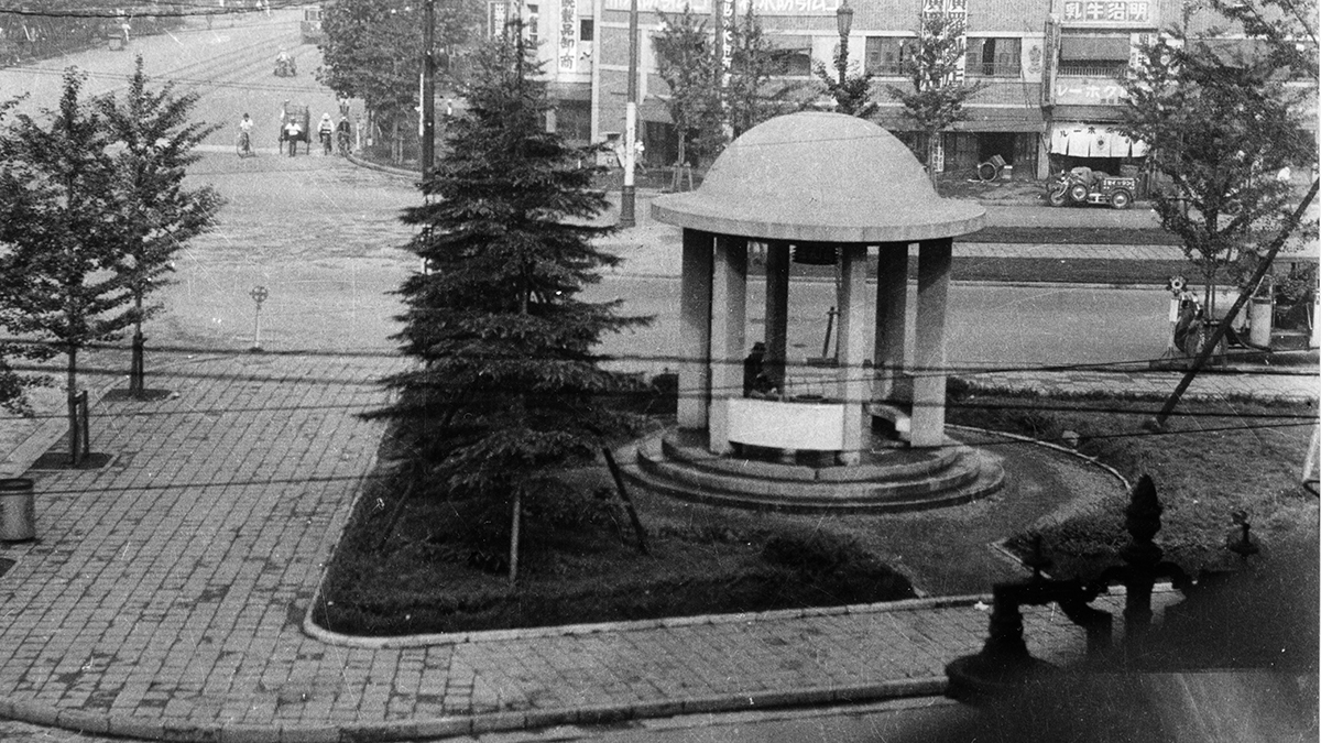 岩本町三丁目町会・岩三史委員会編『岩三史』2ページより引用した、昭和15年（1940年）頃の岩本町交差点の写真です。現在「馬の水飲み広場」と呼ばれている三角地帯の写真です。三角地帯の中心に古代ローマ風のガゼボ（gazeb　西洋風あずまや）が建っています。当時この場所は「泉廣場（いずみひろば）」「和泉橋廣場公園」（いずみばしひろば）に呼ばれていました。この写真は岡田邦男様からご提供いただきました。