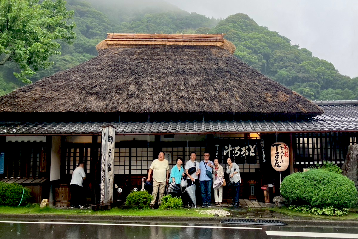 江戸時代の東海道、あの有名な丸子宿の超有名店。あの安藤広重が浮世絵に描いた、永谷園のお茶漬けの袋に入っているカードなアレ、名物とろろ汁、麦飯、むかごがおいしい、ご存知「丁子屋」さんの前で記念撮影。江戸時代から変わらない茅葺きの家屋がお店の入り口。台風8号7号が降らせた雨のおかげでなんとも言えない雨情な風景の丁子屋となりました。浮世絵の中に登場したみたいです。2026年6月27日、岩本町三丁目町会の親睦旅行での一幕です。