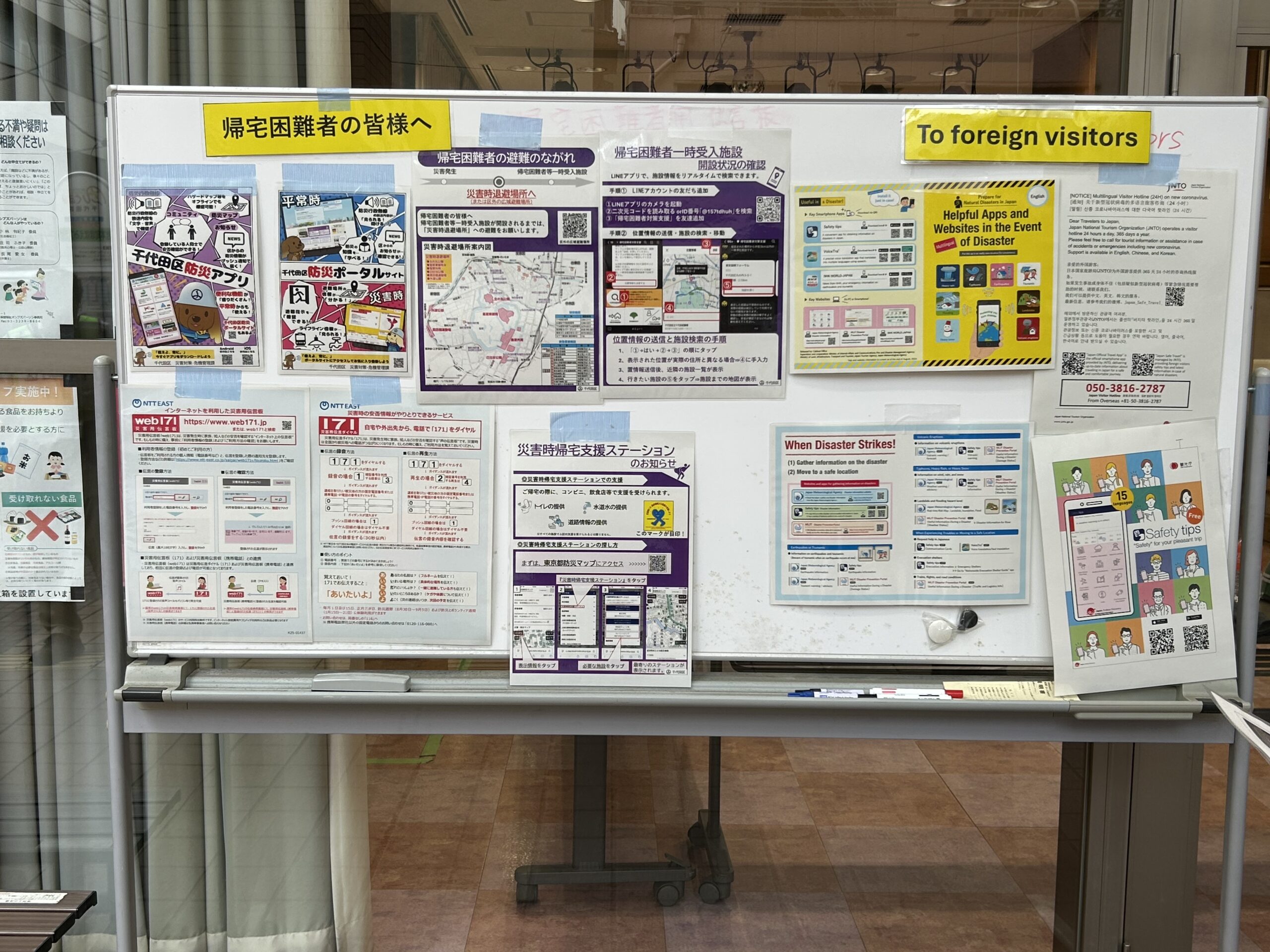 災害時に神田岩本町そして岩本町三丁目等の住民のために開設される「岩本町ほほえみプラザ」避難所の開設訓練で設置した情報掲示板の写真です。帰宅困難者向けの情報（英語版あり）が表示されています。