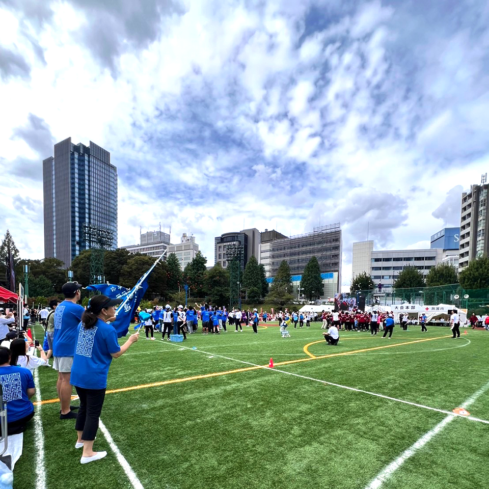第64回千代田区民体育大会が開かれた外濠公園総合グラウンドの様子です。人工芝の広いグランドで玉入れ競技が行われています。岩本町三丁目町会のみなさんも岩本町東神田町会連合会チームの一員として参加しています。青いTシャツを着ている人たちが岩本町東神田町会連合会の皆さんです。